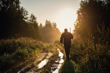 vintage hunter walks the forest road. rifle hunter silhouetted in beautiful sunset or sunrise. hunte