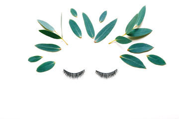 Wall Mural - Female face made of false eyelashes and eucalyptus leaves  on white background