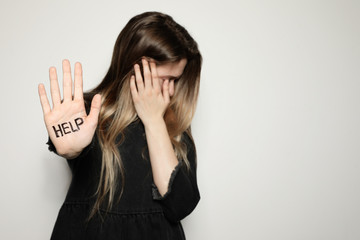 Young woman with word HELP written on her palm against light background, focus on hand. Space for text