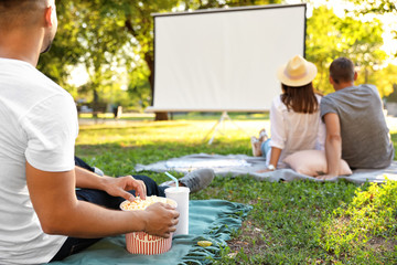 Young man with popcorn watching movie in open air cinema, closeup. Space for text