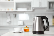 Modern Electric Kettle, Cup And Honey On Wooden Table In Kitchen