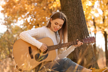 Teen girl playing guitar in autumn park