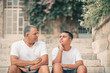 © Inna - Teenager son and senior father sitting on stairs outdoors at home, talking.