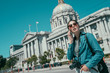 Happy asian young woman in sunglasses calling on smartphone. famous san francisco city hall in the background under blue sky in daytime. elegant tourist girl with camera talking on cellphone.