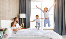 Happy Family Mother, Father And Children Laughing, Playing And Jumping In Bed   At Home