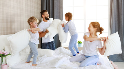 Wall Mural - happy family mother, father and children laughing, playing and jumping in bed   at home