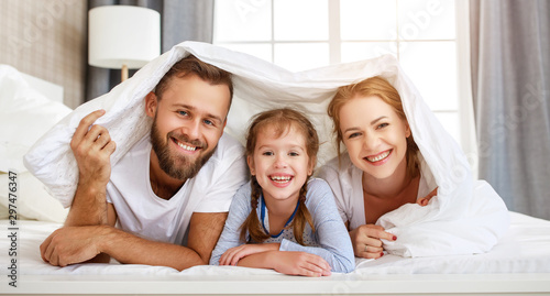 Cuadros en Lienzo happy family mother, father and child laughing, playing and smiling in bed at home