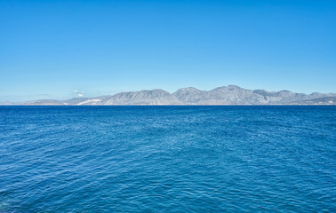 Wall Mural - Calm azure Mediterranean Sea and mountain in horizon. Silhouettes landscape on Greek island Crete.