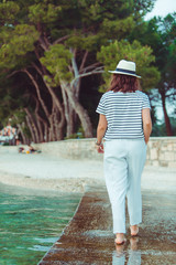 Wall Mural - woman in white clothes and fedora hat walking by sea beach