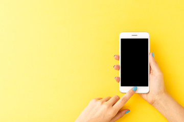 woman’s hands using mobile phone with empty screen on yellow background. top view