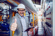 © Dusan Petkovic - Successful caucasian supervisor in suit and with helmet holding tablet and showing thumbs up while standing next to dashboard in power plant.