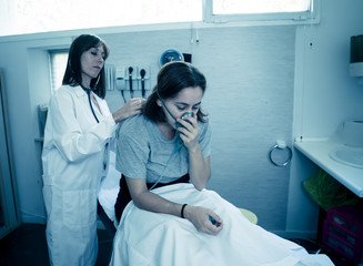 Wall Mural - Sick woman Inhaling through Oxygen Mask having a medical exam by female doctor at hospital