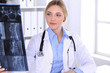 © rogerphoto - Doctor woman examining x-ray picture near window in hospital. Surgeon or orthopedist at work. Medicine and healthcare concept. Blue colored blouse of a therapist looks good