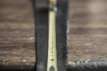 Wall Mural - Close-up, shallow focus of an extended measuring tape showing the scales. Also are an old hammer and wood saw seen on an old, wooden workshop table.