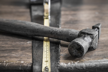 Wall Mural - Close-up, shallow focus of an extended measuring tape showing the scales. Also are an old hammer and wood saw seen on an old, wooden workshop table.