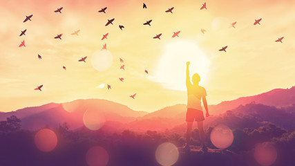 Wall Mural - Freedom feel good and travel adventure concept. Copy space of silhouette man rising hands on sunset sky at top of mountain and bird fly abstract background.