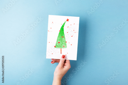 Overhead view on female's hands holding card with a painted Christmas tree on...