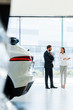 © LIGHTFIELD STUDIOS - selective focus attractive car dealer gesturing near bearded man in car showroom