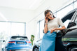 © LIGHTFIELD STUDIOS - attractive and pensive woman standing near cars in car showroom
