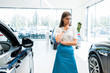 © LIGHTFIELD STUDIOS - young and pensive woman standing near cars in car showroom