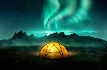 a glowing yellow camping tent under a beautiful green northern lights aurora. travel adventure lands