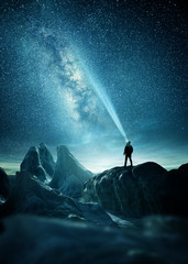 Wall Mural - the milky way lighting up the night sky with a man shining a flashlight towards it. photo composite.