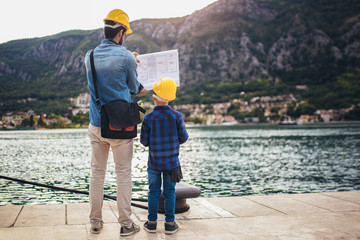 Harbor engineer with his son holding the paper, construction work, smiling.