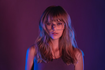 Wall Mural - Fashion sexy young woman 20s girl model attractive face blond hairstyle wearing stylish trendy eyewear sunglasses looking at camera at purple violet neon light studio background, closeup portrait