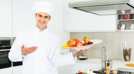 Wall Mural - Portrait of man cook who is standing with fruits on his work place in the kitchen