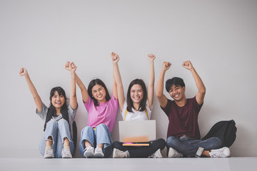 Education concept - Group of cheerful students sat on the floor against a laptop computer and celebrated their team success on a soft background.