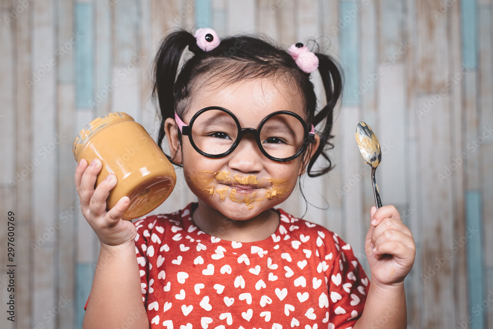 little asian girl holding and enjoying peanut butter in jar and a spoon, Concept of peanut butter lover