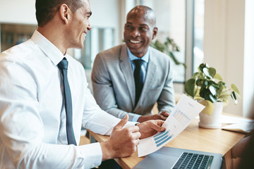 two smiling diverse businessmen discussing graphs together in an