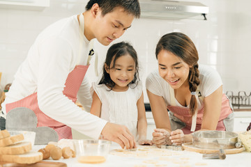 Young asian family cooking food in kitchen.Happy Little girl with her father and mother mixing batter.mother and Little girl preparing the dough.Happy family in the kitchen and junior chef Concept.