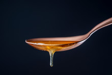 Thick Honey Dripping From The One Metal Spoon On Black Background, Close Up. Honey Flowing From Spoon