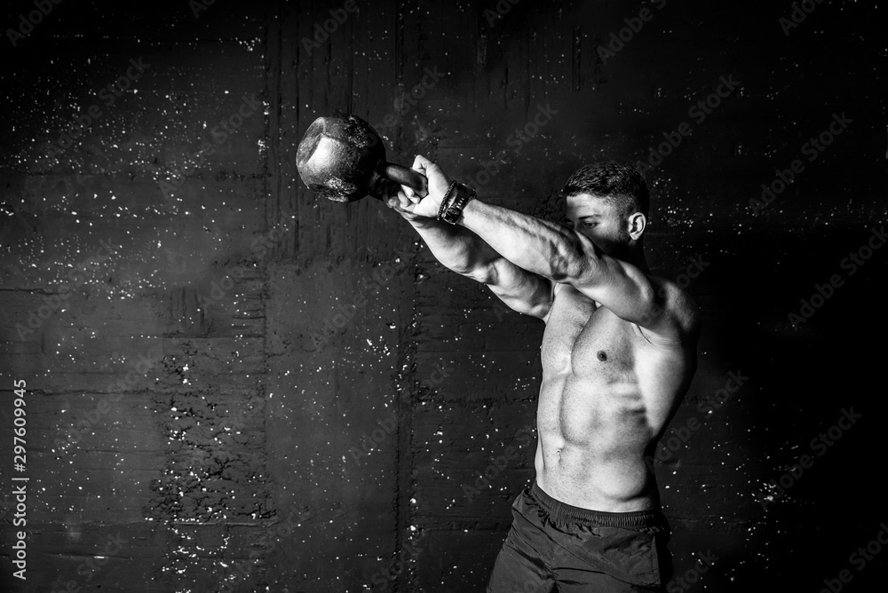 Young strong sweaty focused fit muscular man with big muscles holding heavy kettle bell for swing cross training hard core workout in the gym black and white - obrazy, fototapety, plakaty 