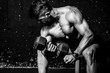 © Srdjan - Young strong muscular sweaty fit man biceps muscle workout cross training with heavy dumbbell in the gym dark image with shadows real people black and white