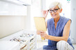 Beautiful mature woman choosing new pair of spectacles in opticians store. Eyesight correction.