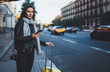 Traveler woman with suitcase calling mobile phone waiting yellow auto taxi in evening street europe city Barcelona. Girl tourist using smartphone technology internet online gadget cellphone