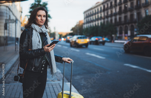 Cuadros en Lienzo Traveler woman with suitcase calling mobile phone waiting yellow auto taxi in evening street europe city Barcelona