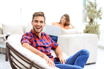 Wall Mural - happy young man sitting in a big chair on blurred background