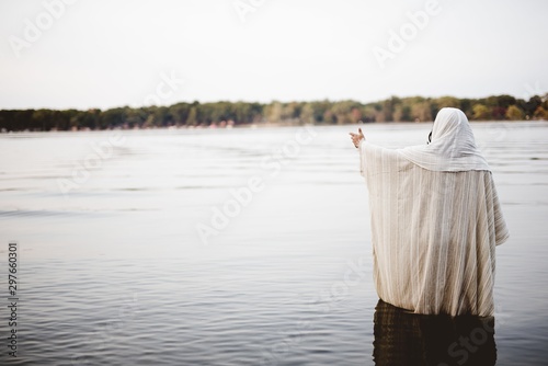 Fotografía Person wearing a biblical robe standing in the water with a hand up