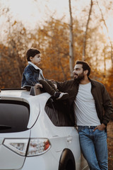 Wall Mural - Happy father stanting near the car with his son sitting on car roof.