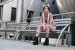 © brillianata - Young woman with futuristic looks sitting on a bench. Girl with black and white pigtails. Against the background of a futuristic building