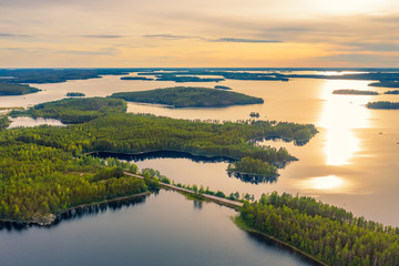 Wall Mural - Aerial view of road between green summer forest and blue lake in Finland. Summer sunset lanscape