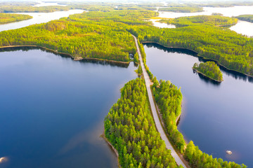 Canvas Print - Aerial view of road between green summer forest and blue lake in Finland
