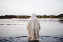 Person Wearing A Biblical Robe Walking In The Water With A Blurred Background Shot From Behind