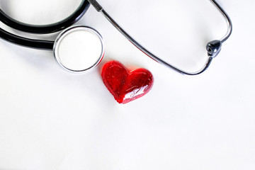 red heart next to medical stethoscope on white background close up