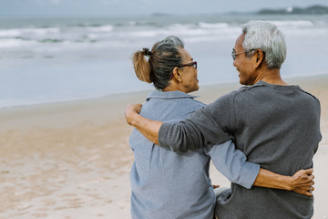 Asian senior couple or elderly people walking and siting at the beach on their weekend vacation holiday. Retirement vaction concept.