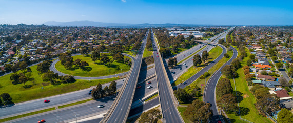 Straight road passing through interchange and leading to mountains in the distance. Aerial view in Melbourne, Australia