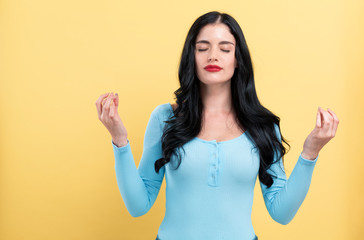 Young woman in a meditation pose on a yellow background